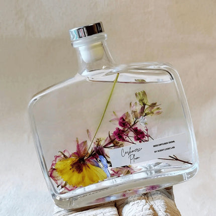 Urbn-cart handmade botanical reed diffuser with dried flowers in a clear glass bottle. Features a silver cap and a label reading 'Cashmere Plum'.