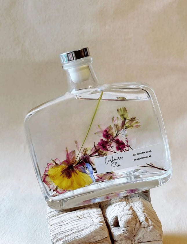 Urbn-cart handmade botanical reed diffuser with dried flowers in a clear glass bottle, silver cap, and 'Cashmere Plum' label.